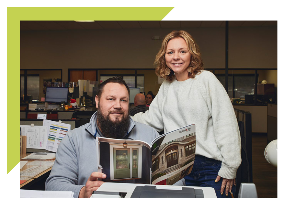 two people in office smiling for a picture while looking at flipping book magazine